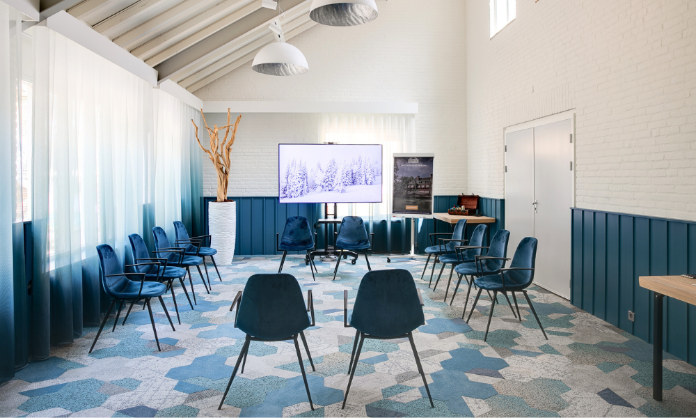 Een moderne vergaderruimte met blauwe stoelen, een groot scherm en lichtblauwe en witte muren.