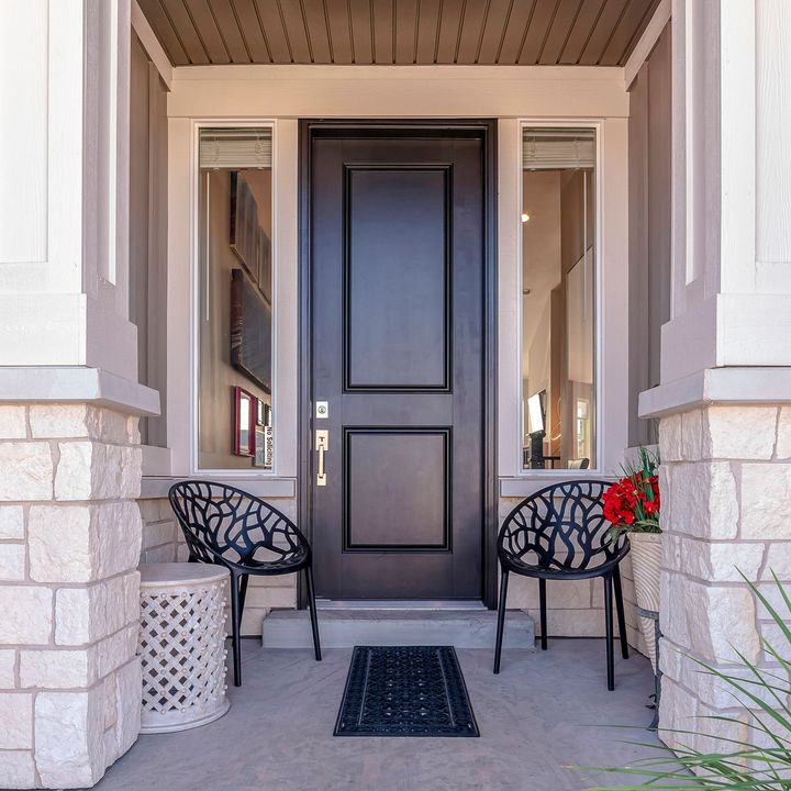 Entrée principale avec porte noire, fenêtres, chaises et colonnes en pierre.