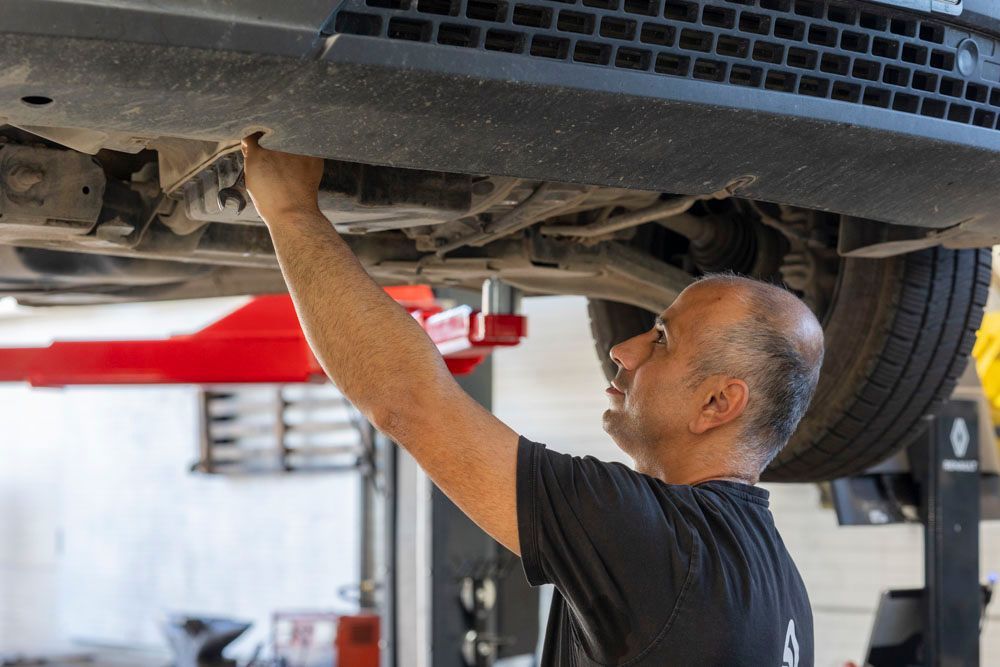 Ein Mechaniker untersucht die Unterseite eines auf einer Hebebühne stehenden Autos in einer Autowerkstatt.