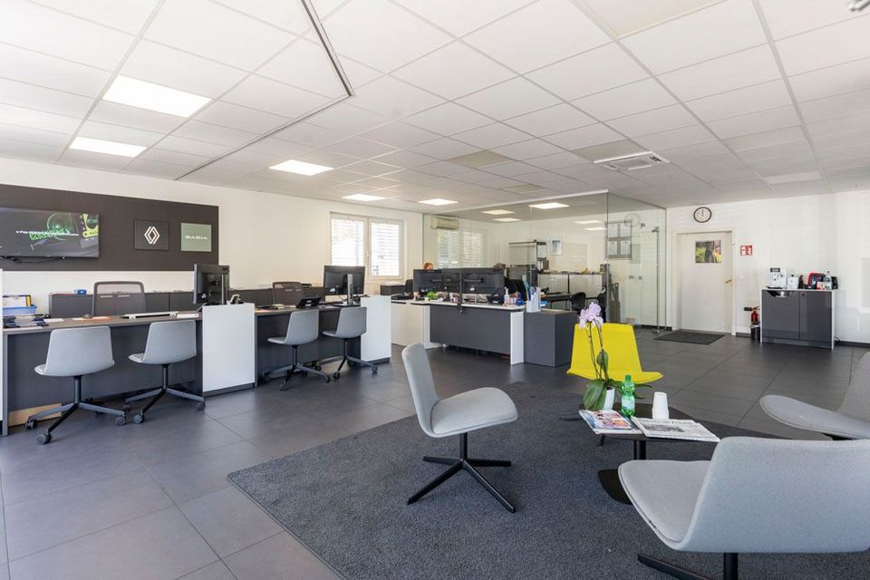 Moderne Bürolounge mit Schreibtischen, Stühlen, dunklem Teppichboden und einem hellen, offenen Arbeitsbereich