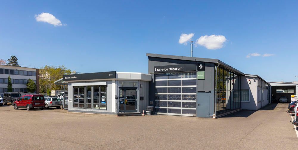 Modernes Autowerkstattgebäude mit gläserner Schaufensterfront, Garagentoren und geparkten Autos unter blauem Himmel