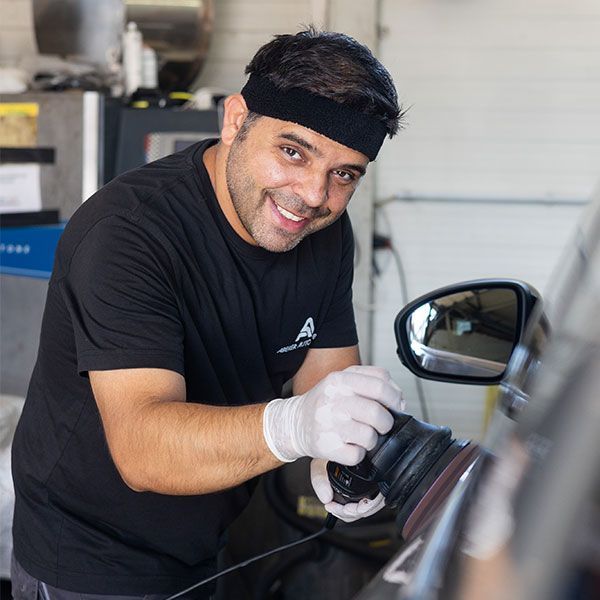 Ein Mechaniker lächelt, während er in einer Autowerkstatt ein Auto poliert.