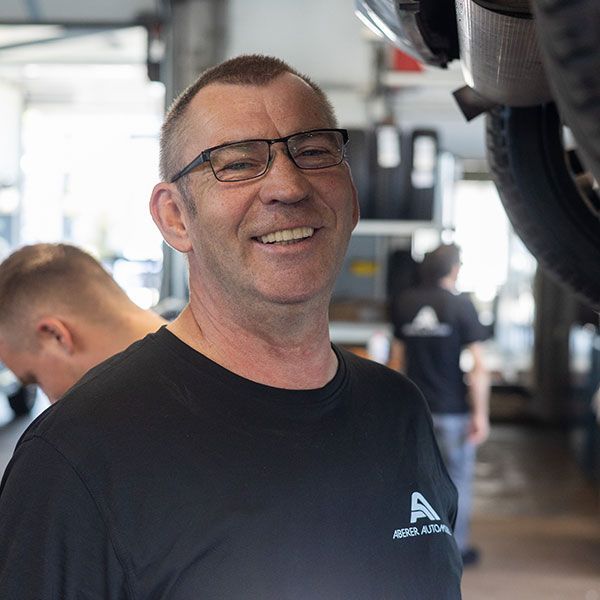 Lächelnder Mann mit Brille und schwarzem Hemd in einer Turnhalle oder Autowerkstatt