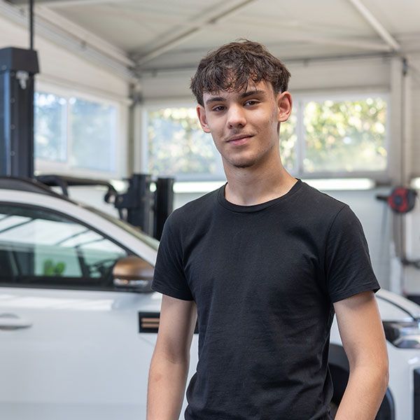 Junger Mann in einem schwarzen T-Shirt steht in einer Garage neben einem weißen Auto