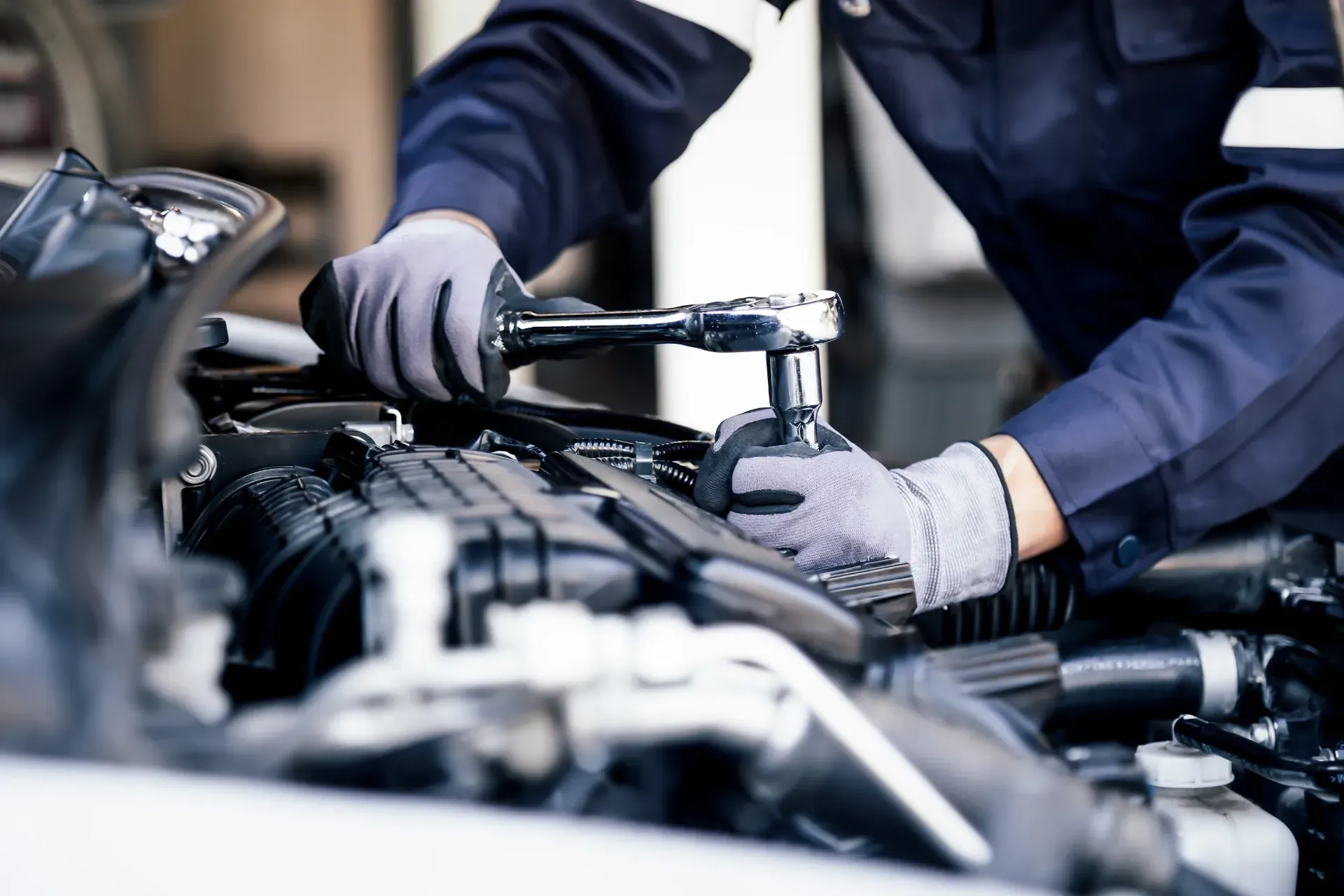 Ein Mechaniker mit Handschuhen arbeitet in einer Garage an einem Automotor.