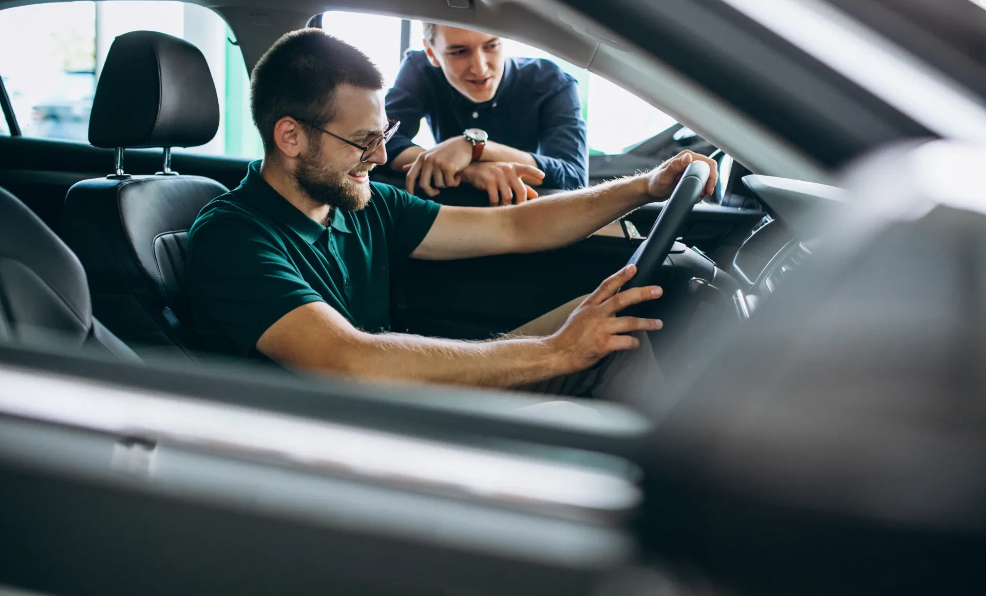 Zwei Personen in einem Auto, eine fährt und lächelt, während die andere sich über den Sitz beugt und nach vorne zeigt.