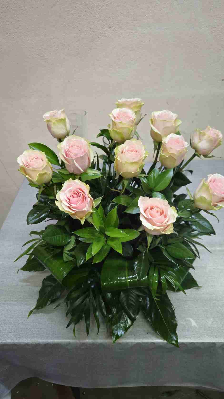 Rosas rosadas en un arreglo floral con hojas verdes, sobre una mesa.