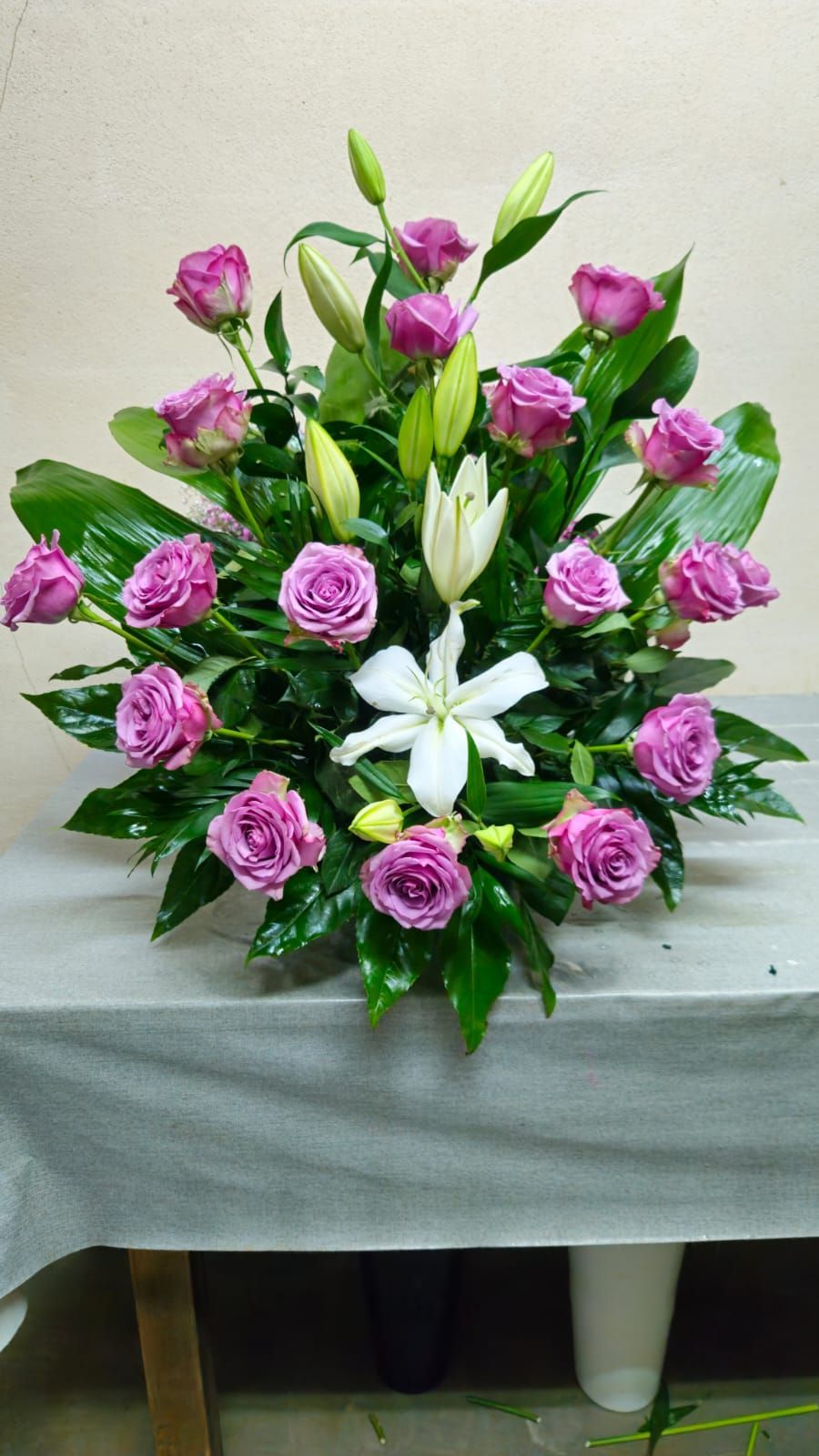 Arreglo floral de rosas moradas y lirios blancos sobre una mesa.