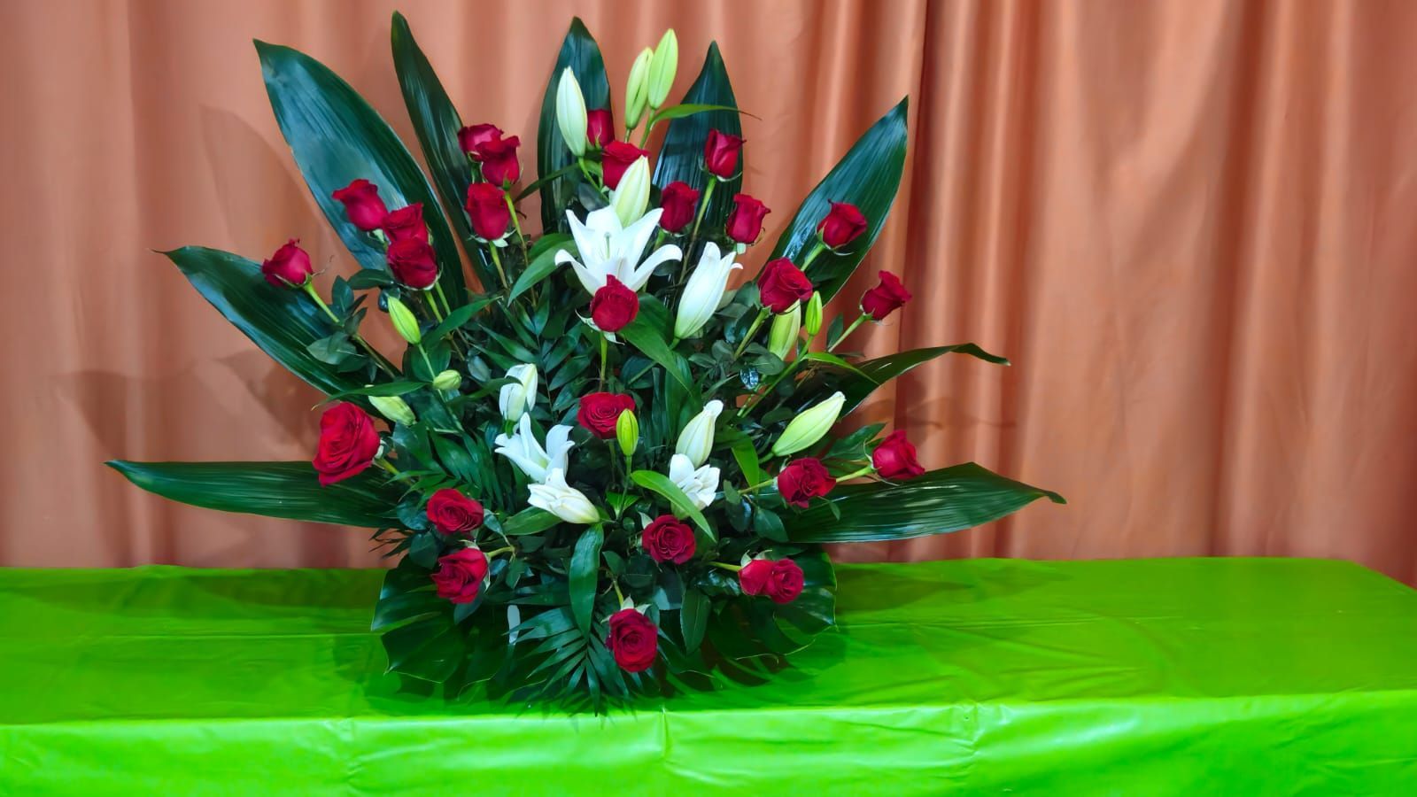 Arreglo floral de rosas rojas y lirios blancos sobre una superficie verde.