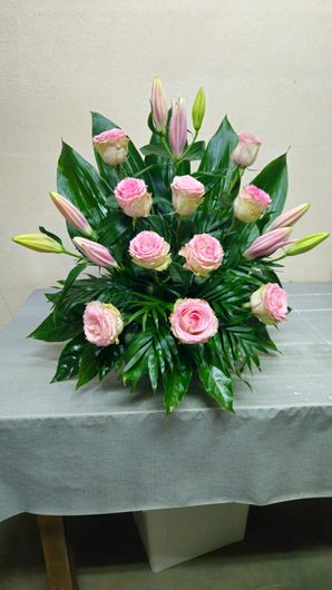 Arreglo floral con rosas rosadas y lirios, vegetación, sobre una mesa.