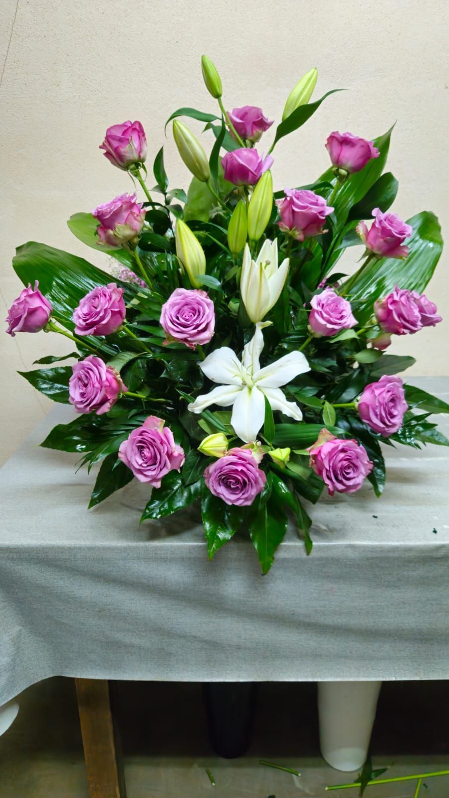 Arreglo floral: rosas lavanda, lirios blancos y follaje verde. Sobre una mesa, para interior.