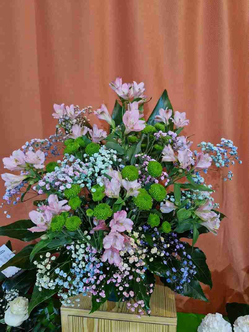 Arreglo floral de alstroemerias rosas, crisantemos verdes y gipsófilas azules en una canasta tejida.