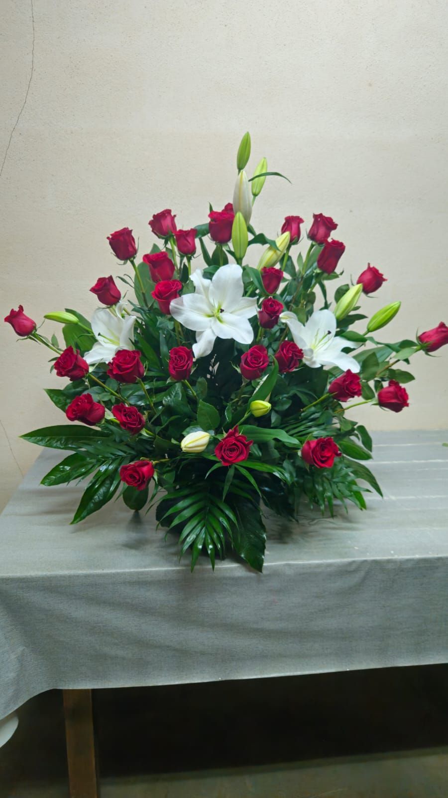 Arreglo floral de rosas rojas y lirios blancos sobre una mesa gris.