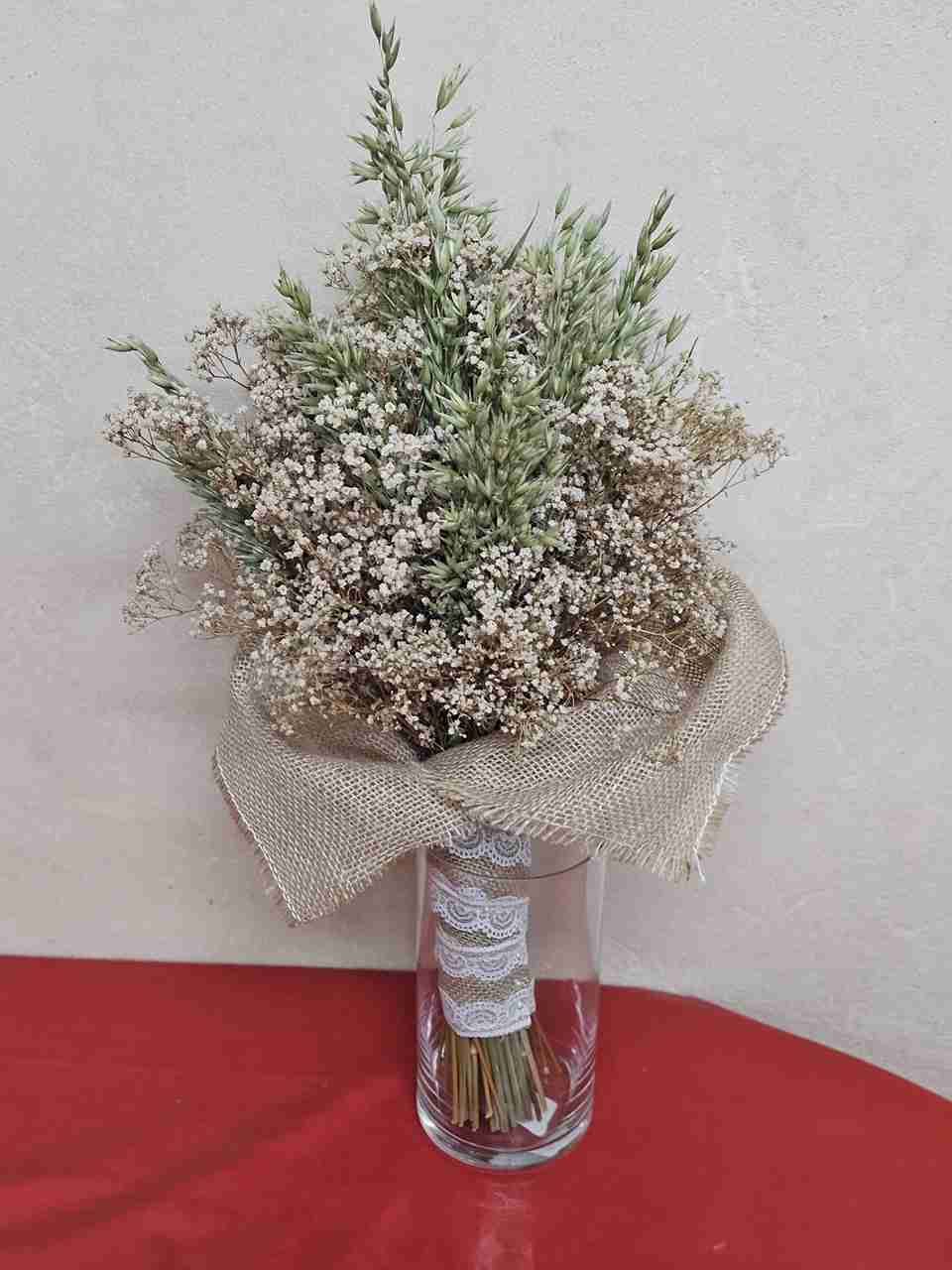 Ramo de flores secas en jarrón de cristal, envuelto con arpillera y encaje.