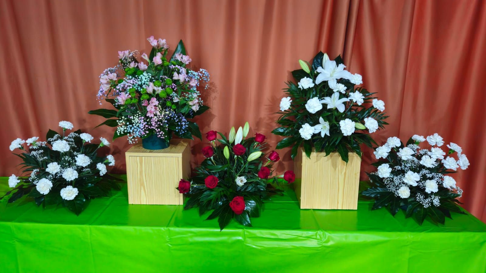 Cinco arreglos florales sobre una mesa verde frente a un fondo color melocotón.