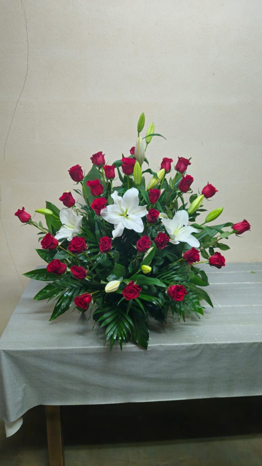 Rosas rojas y lirios blancos en un arreglo floral sobre una mesa.
