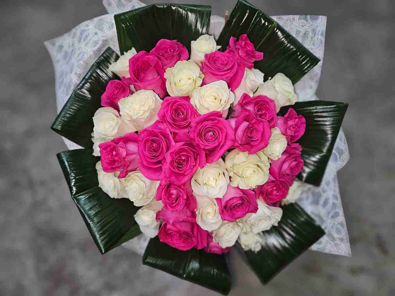 Ramo de rosas rosas y blancas, con hojas verdes y papel blanco.