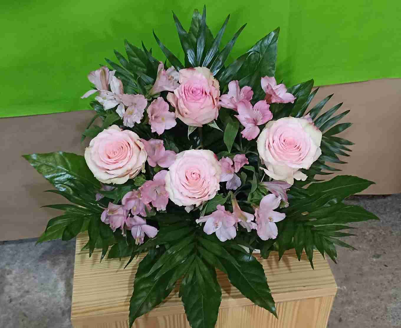 Rosas rosadas y lirios dispuestos en una exhibición floral con follaje verde.