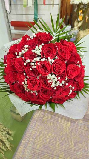 Ramo de rosas rojas y gitanos, envuelto en papel blanco, con follaje verde.