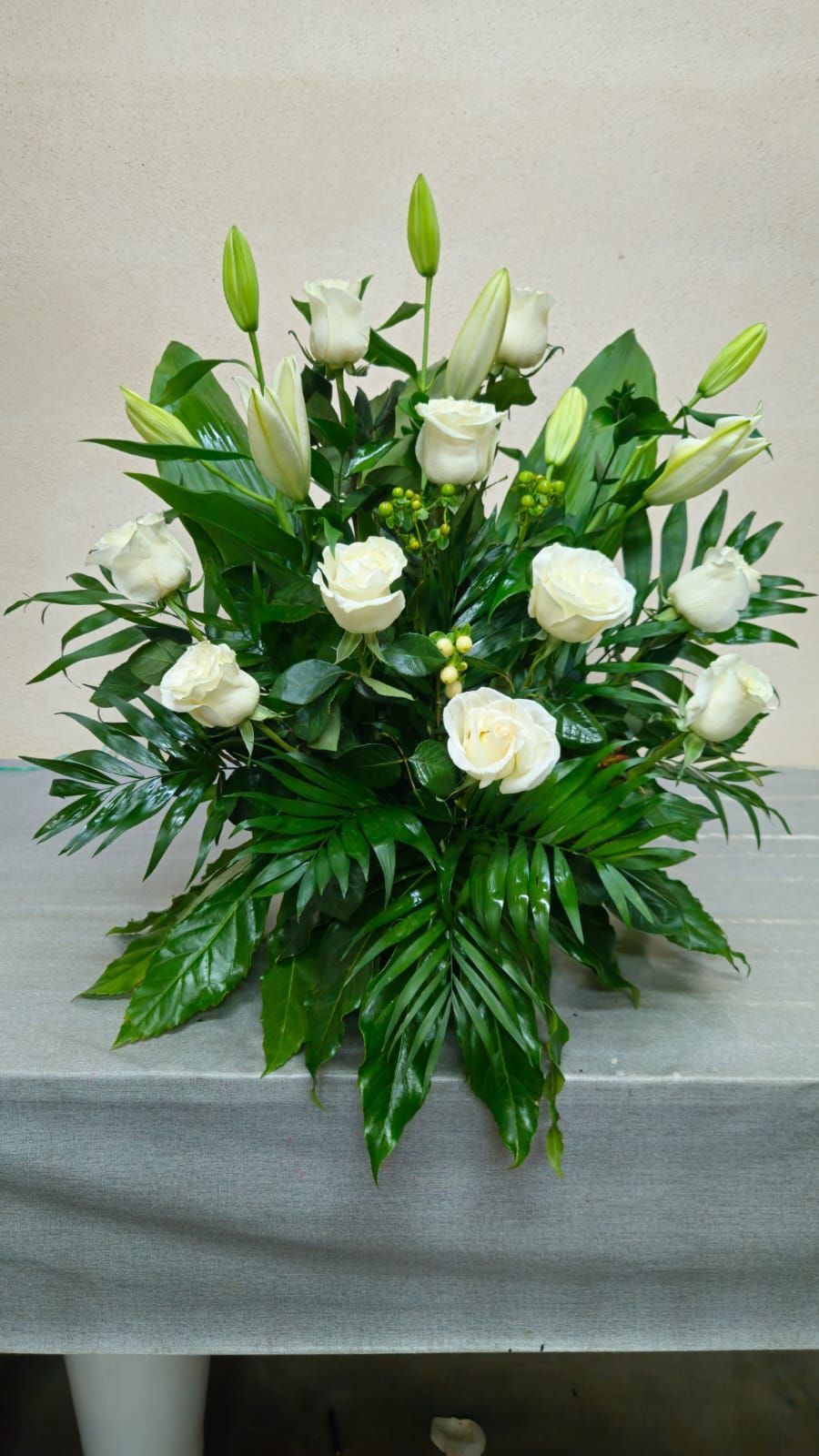 Rosas blancas y lirios en un arreglo floral con hojas verdes sobre una mesa.