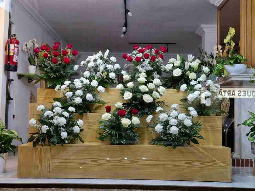 Exhibición floral con rosas rojas y blancas sobre estantes de madera escalonados.