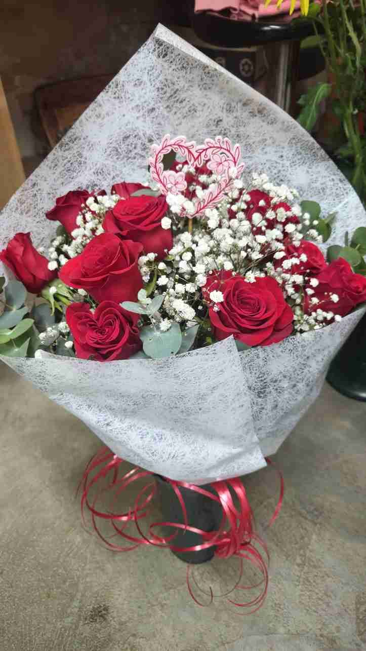 Ramo de rosas rojas, gitanos y follaje, envuelto en papel blanco, atado con cinta roja y rematado con un corazón.