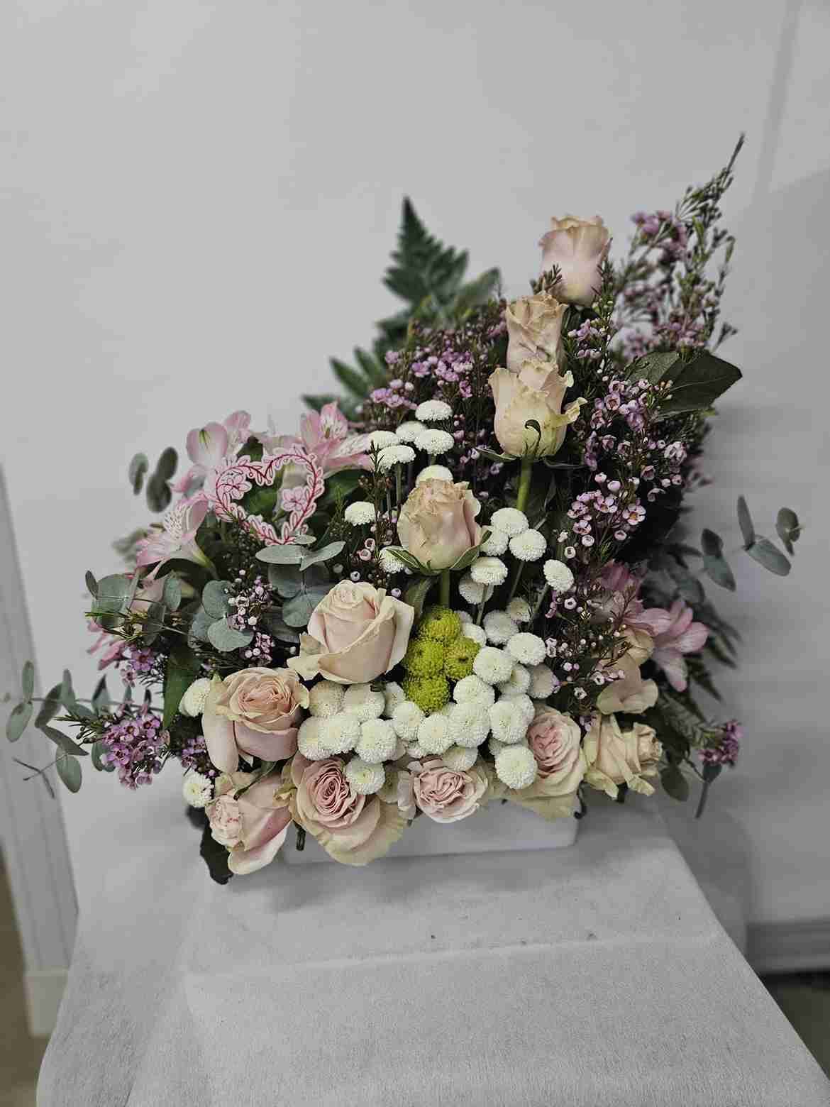 Arreglo floral de rosas de color rosa pálido, flores blancas y vegetación.