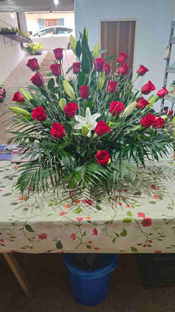 Rosas rojas y lirios blancos en arreglo floral sobre mantel estampado.