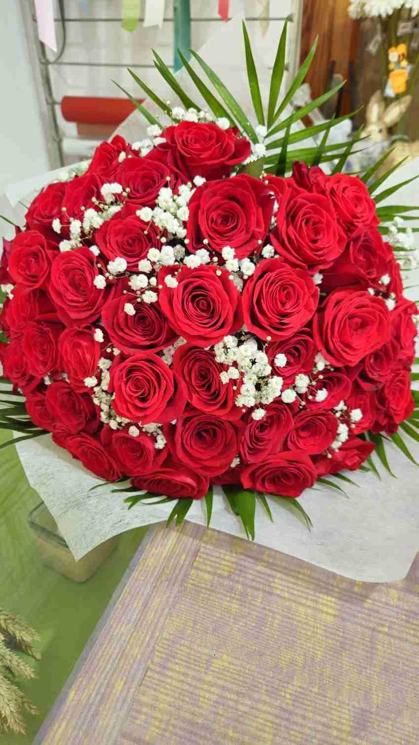 Rosas rojas dispuestas en un ramo con flores de aliento de bebé y follaje verde.