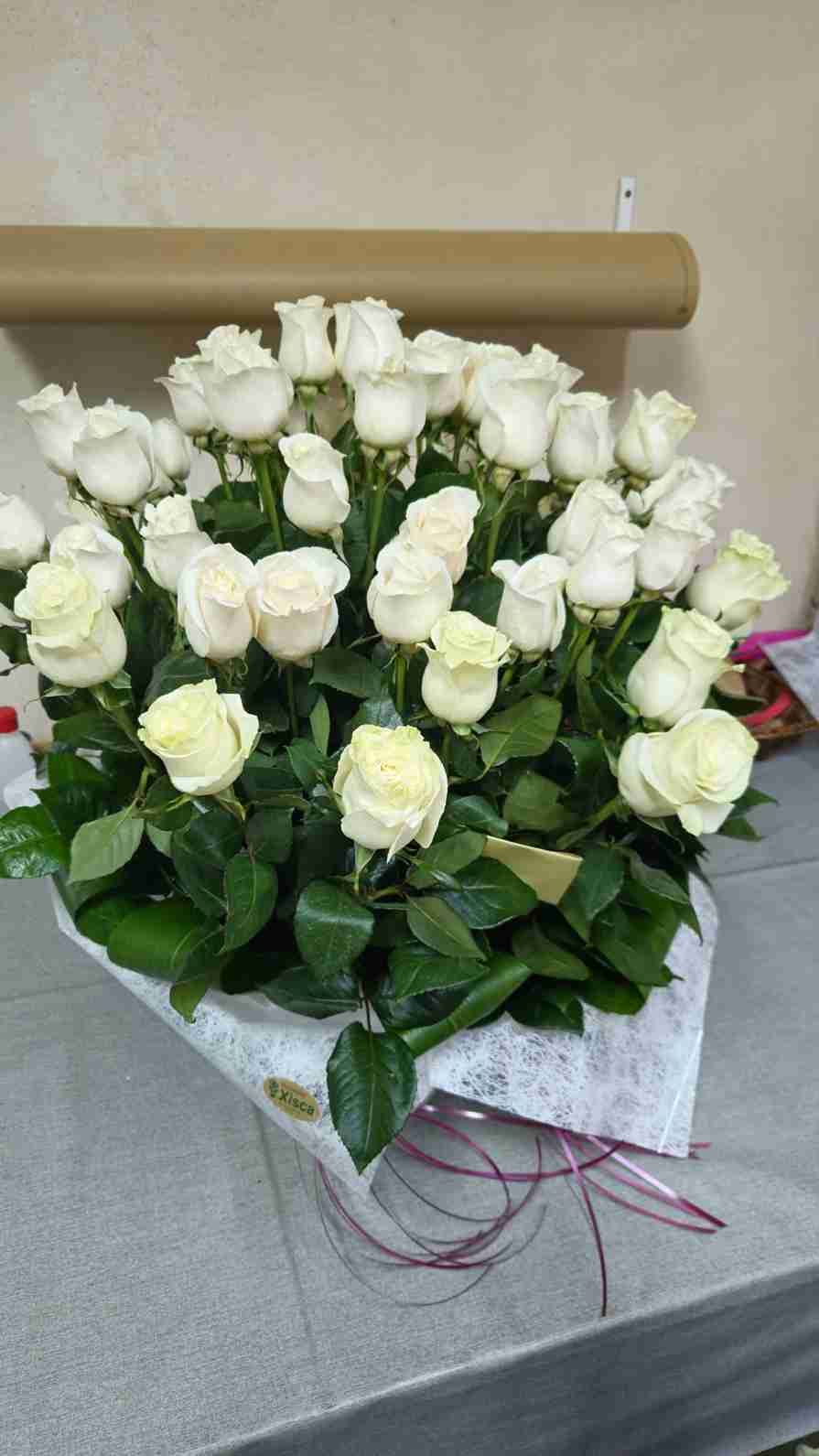 Ramo de muchas rosas blancas, envuelto en papel, sobre una superficie gris.