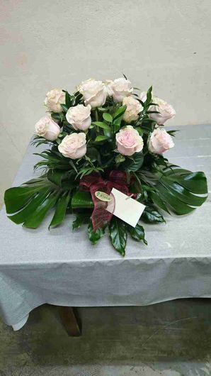 Arreglo de rosas de color rosa pálido, hojas verdes y una tarjeta sobre una mesa.