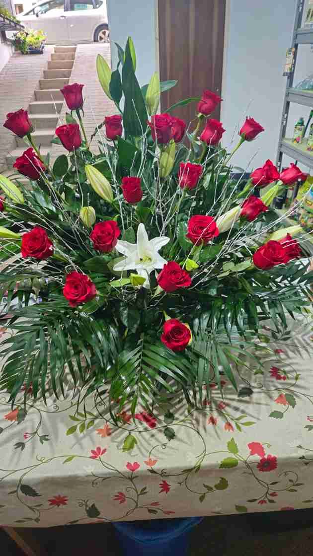 Arreglo floral con rosas rojas y lirios blancos sobre mantel estampado.