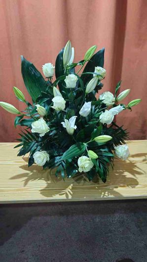 Arreglo floral de rosas blancas y lirios sobre una superficie de madera.