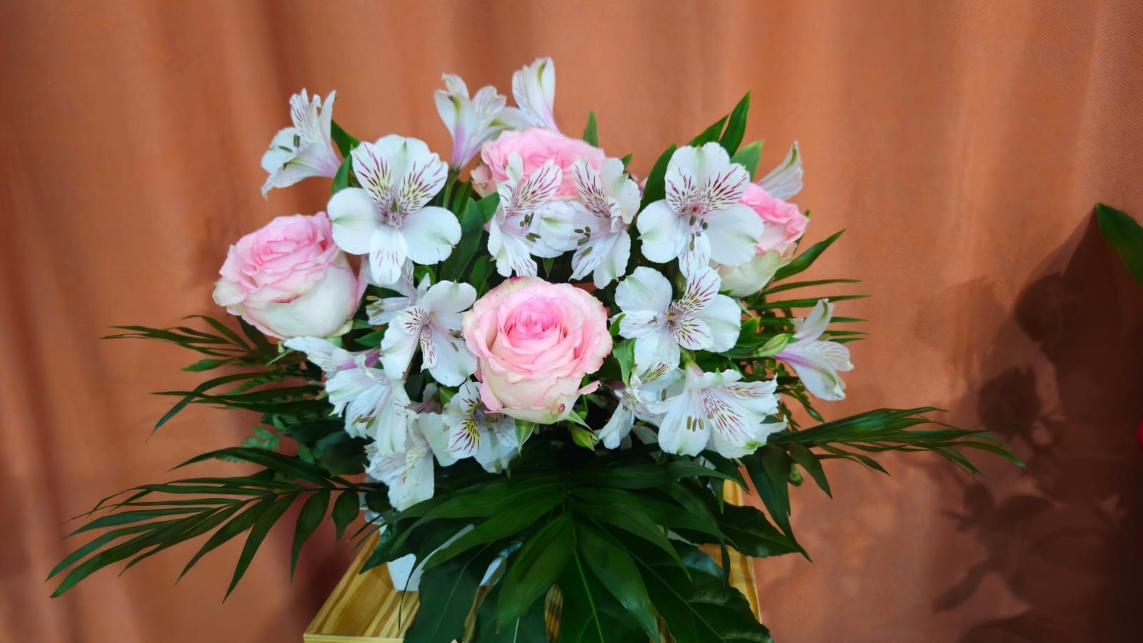 Ramo de rosas rosadas y lirios blancos con follaje verde sobre un fondo de melocotón.