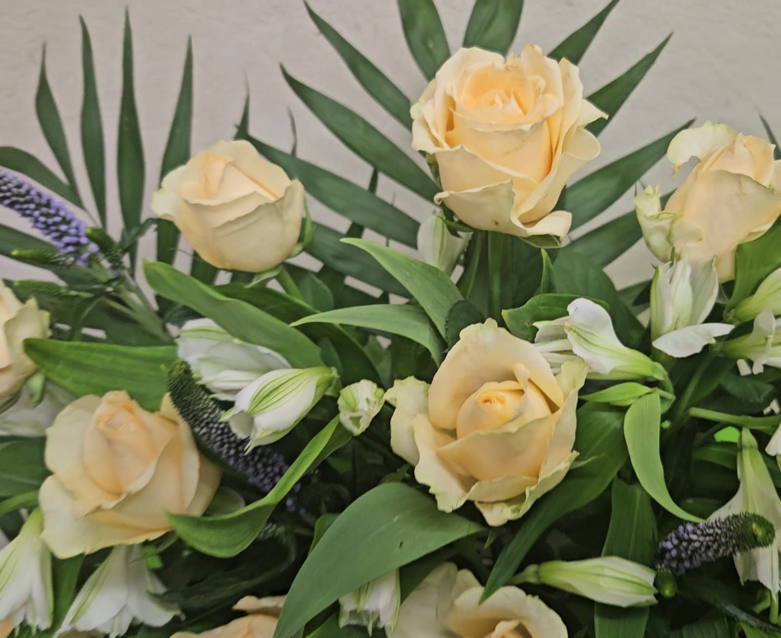 Rosas de color crema y lirios blancos en un arreglo floral con follaje verde.