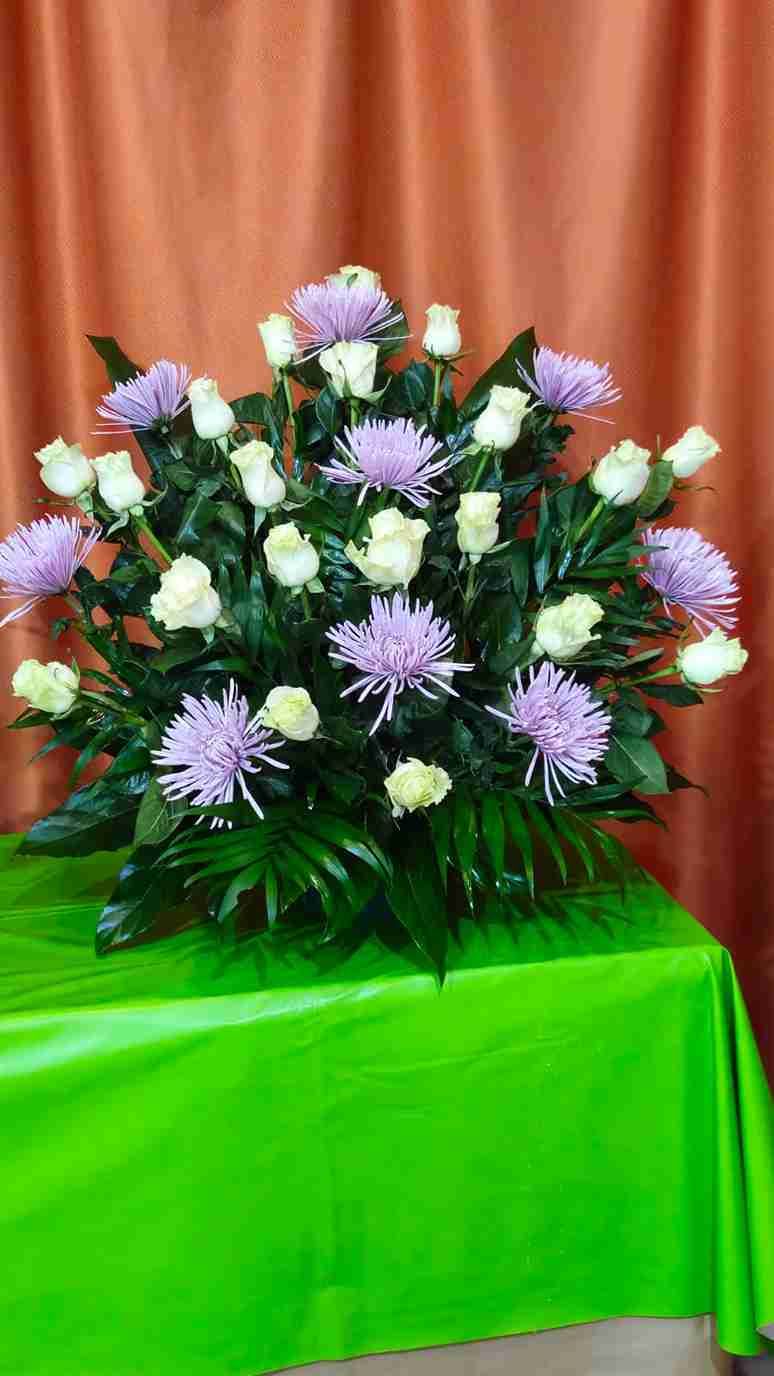 Arreglo floral de rosas blancas y crisantemos morados sobre una mesa verde con fondo naranja.