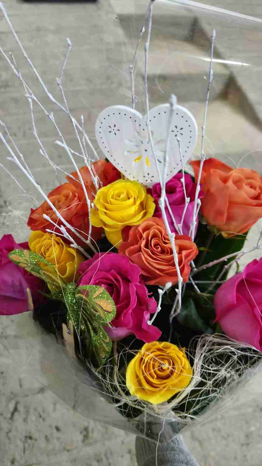 Ramo de rosas de colores: naranjas, amarillas, rosas, con decoración de corazón blanco.