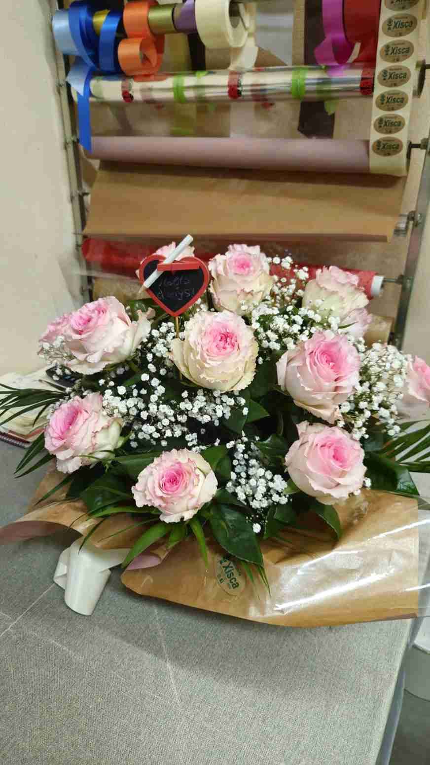 Ramo de rosas rosas y gitanos en floristería, envuelto en papel marrón con un pequeño corazón.