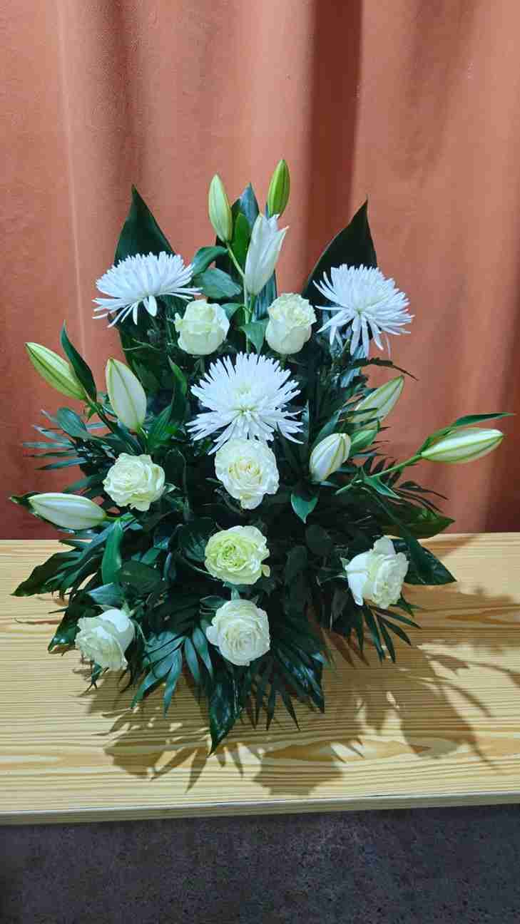 Arreglo floral blanco sobre una superficie de madera, con lirios, rosas y crisantemos sobre un fondo marrón.