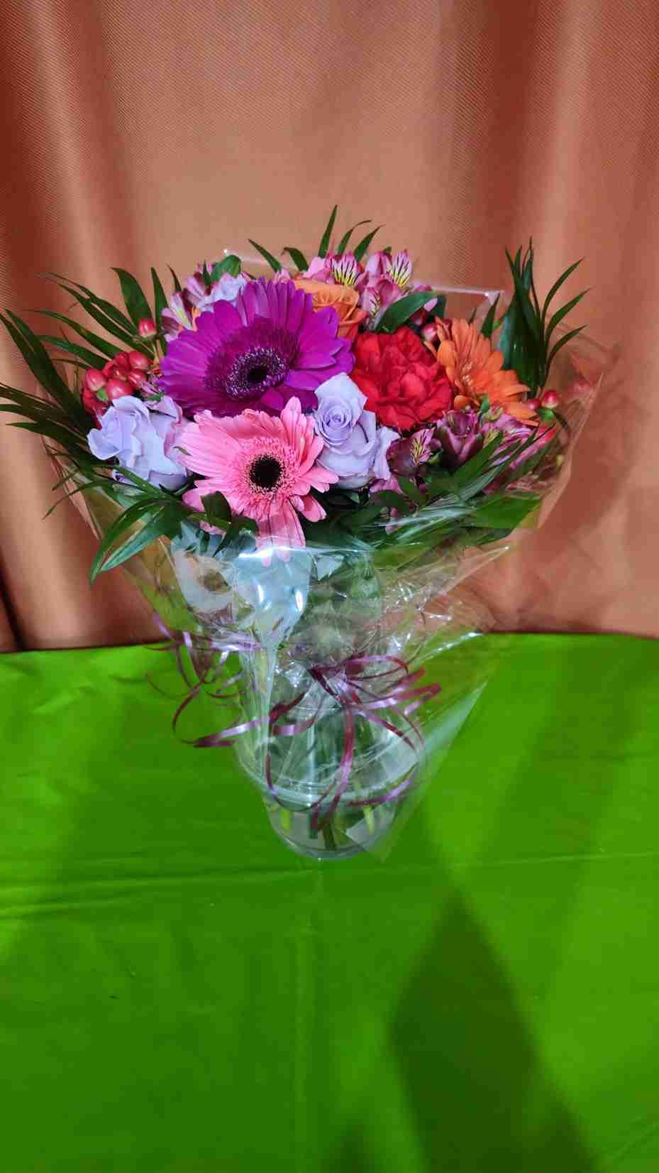 Ramo de flores de colores envuelto en celofán transparente sobre una superficie verde.