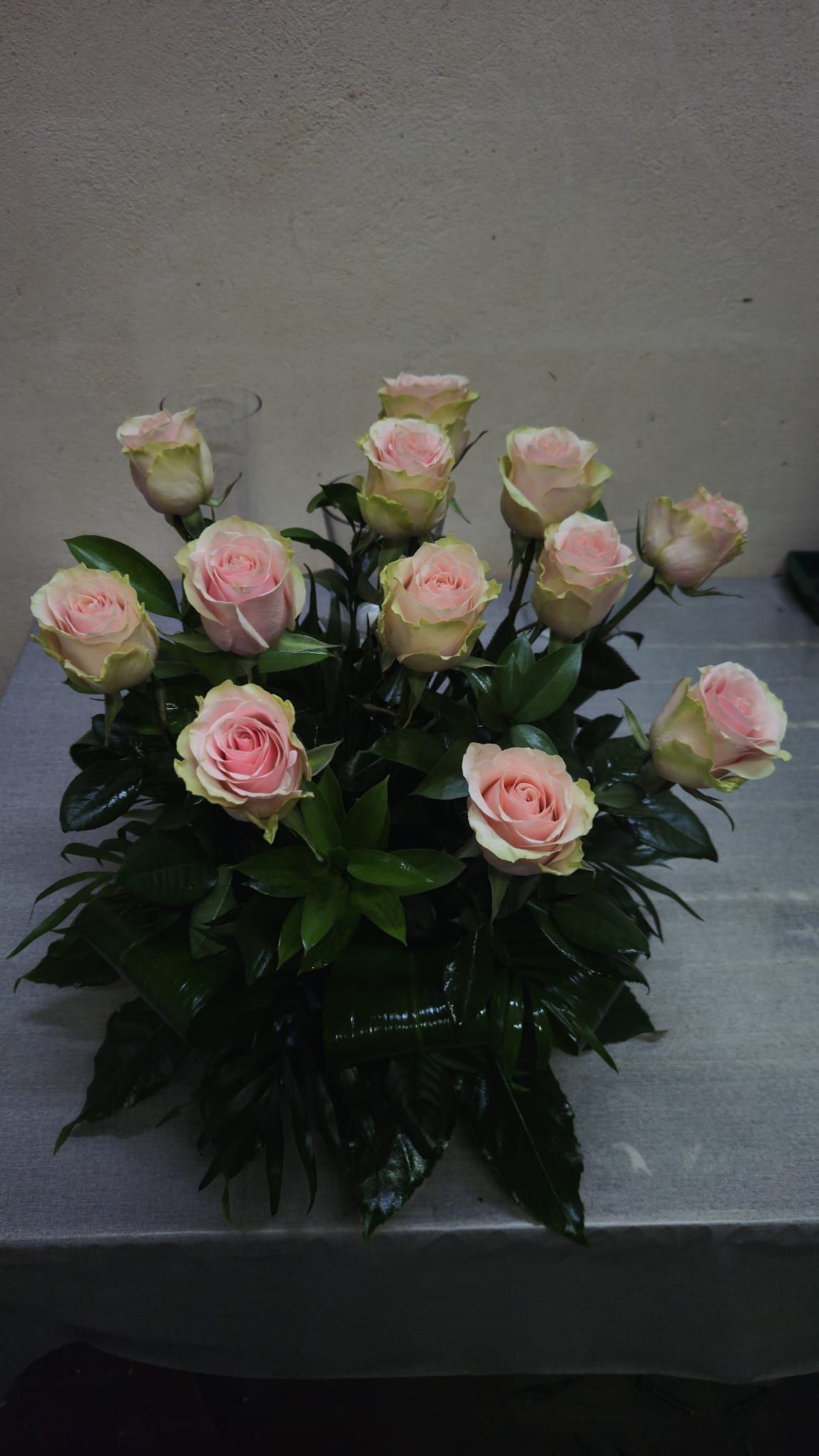 Rosas rosadas arregladas con hojas verdes sobre una mesa.