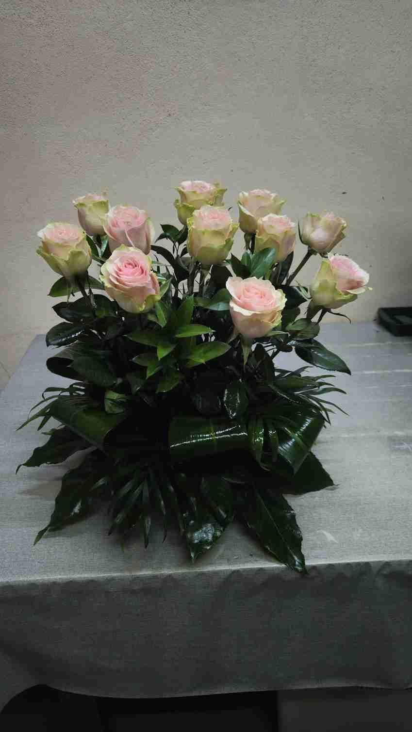 Arreglo floral: rosas de color rosa y crema con hojas verdes, expuestas sobre una superficie gris.