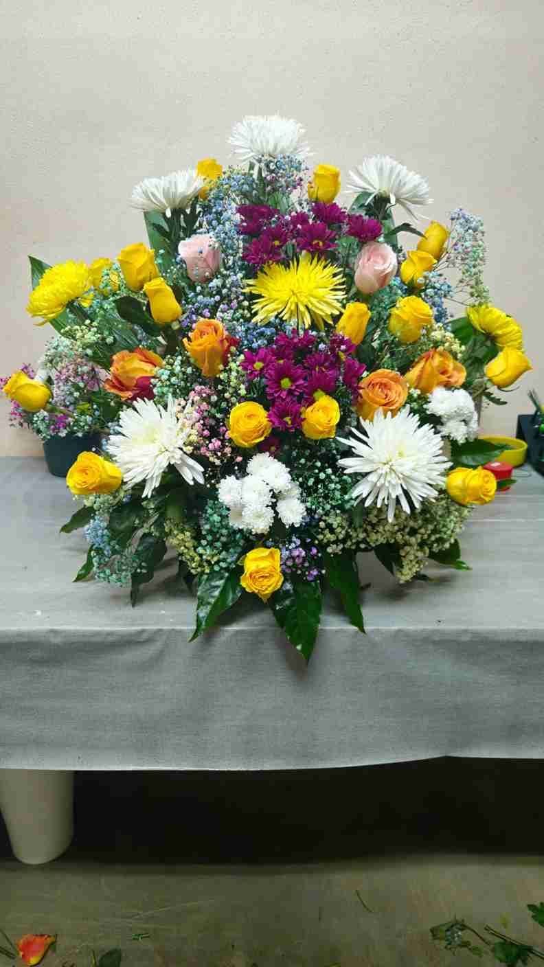 Arreglo floral colorido: rosas amarillas, crisantemos blancos, flores de naranja y acentos azules.