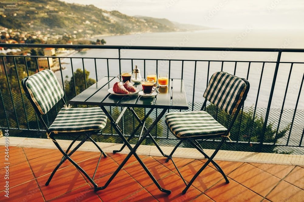 Ein zum Frühstück gedeckter Tisch mit Kaffee und Gebäck auf einer Terrasse mit Blick auf eine malerische Küste und das Meer.