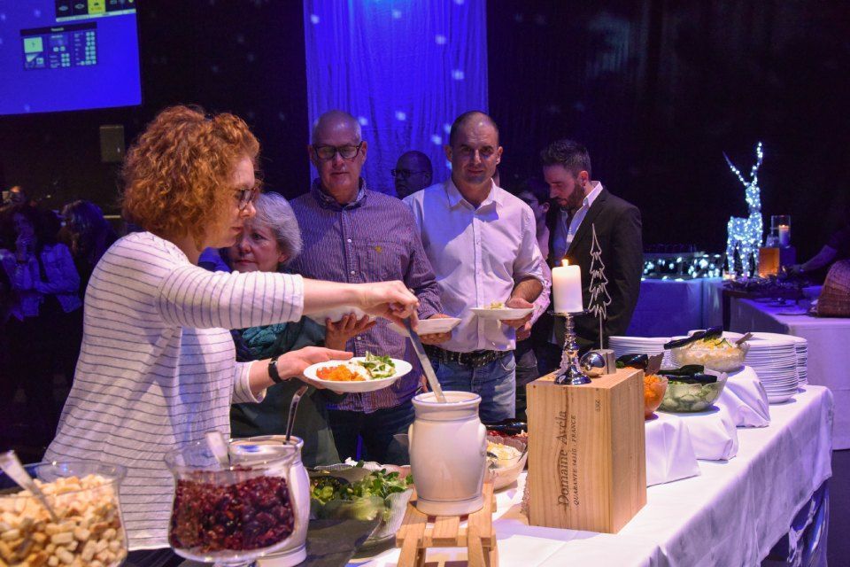 Eine Frau serviert Essen von einem Buffet an Menschen, die in einem schwach beleuchteten, blau erleuchteten Veranstaltungsraum Schlange stehen.