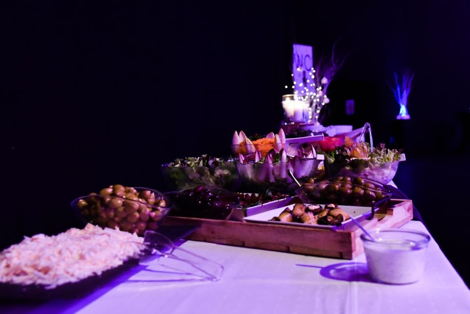 Ein Buffet mit Schüsseln voller Vorspeisen, Salat und Dip, beleuchtet von violettem Ambientelicht in einem dunklen Raum.