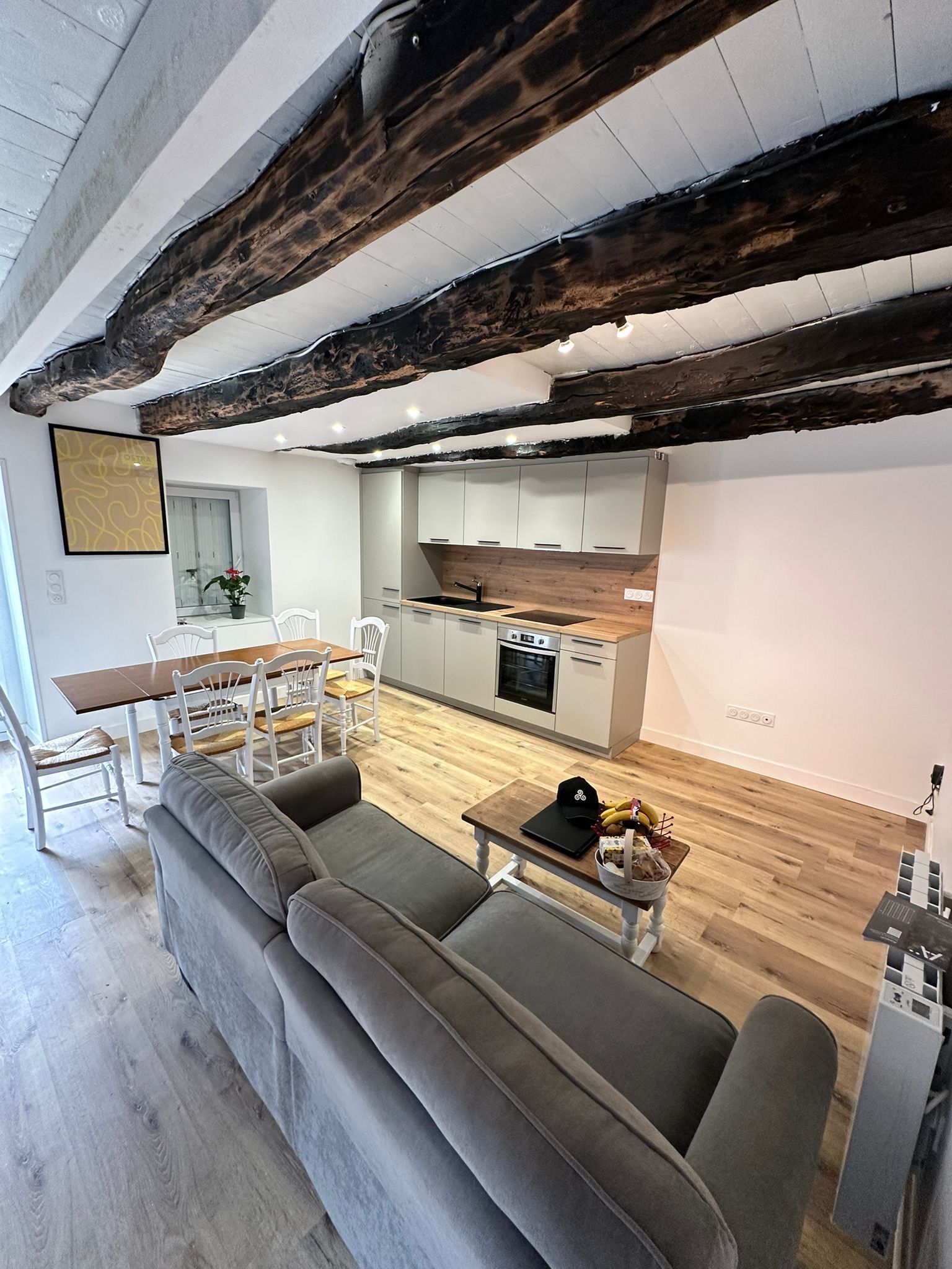 Séjour avec cuisine, table à manger, canapé et poutres en bois.