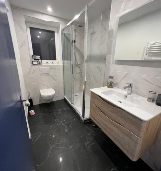 Salle de bain moderne avec carrelage noir, douche, vanité, toilettes et fenêtre.