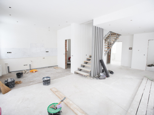 Intérieur d'une maison en rénovation : murs bruts, sols nus, escalier, matériaux de construction.