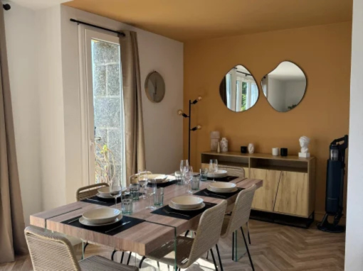 Salle à manger avec des murs couleur moutarde, deux miroirs et une table dressée pour six personnes.
